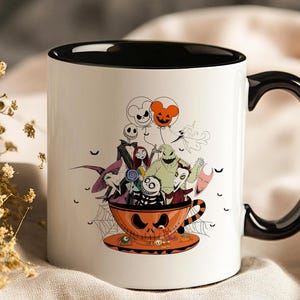 May include: White ceramic mug with a black interior and handle. The mug features a Halloween-themed illustration of characters from The Nightmare Before Christmas, including Jack Skellington, Sally, and Oogie Boogie, inside an orange teacup.