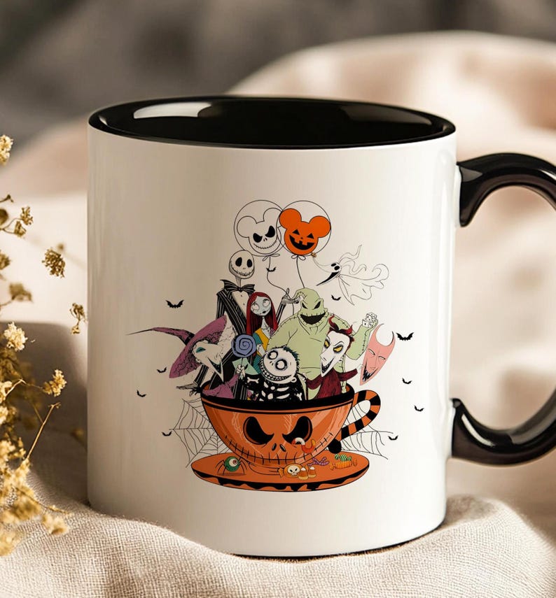 May include: White ceramic mug with a black interior and handle. The mug features a Halloween-themed illustration of characters from The Nightmare Before Christmas, including Jack Skellington, Sally, and Oogie Boogie, inside an orange teacup.