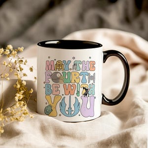 May include: White ceramic mug with a black rim and handle. The mug has a colorful graphic that says "May the Fourth Be With You" with Star Wars characters.
