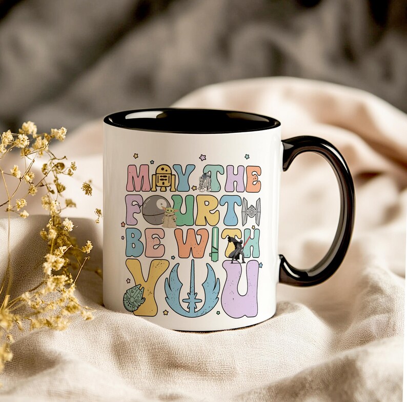 May include: White ceramic mug with a black rim and handle. The mug has a colorful graphic that says "May the Fourth Be With You" with Star Wars characters.