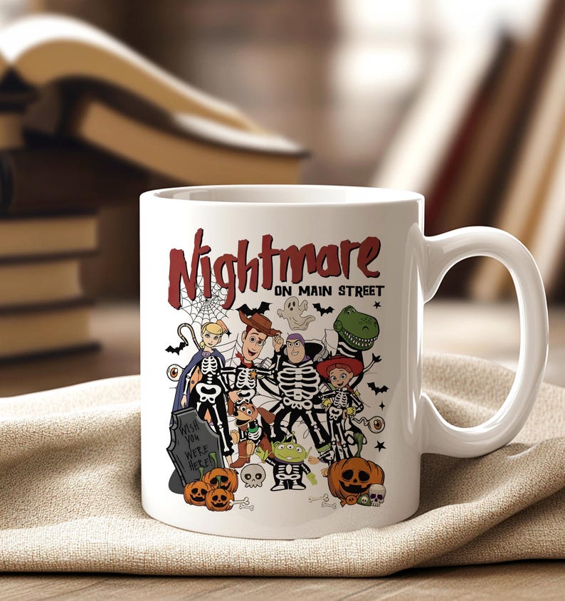 May include: White ceramic mug featuring a Halloween-themed design with the text "Nightmare on Main Street." The design includes cartoon characters dressed as skeletons, pumpkins, and a tombstone. The mug has a curved handle.