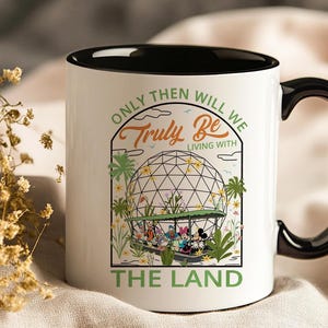 May include: White ceramic mug with a black interior and handle. The mug features a colorful graphic of Disney characters in a boat, with the text "Only Then Will We Truly Be Living With The Land."