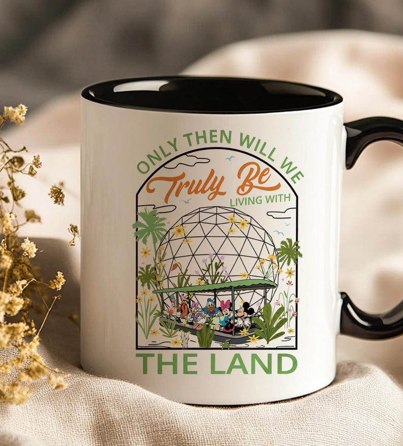 May include: White ceramic mug with a black interior and handle. The mug features a colorful graphic of Disney characters in a boat, with the text "Only Then Will We Truly Be Living With The Land."