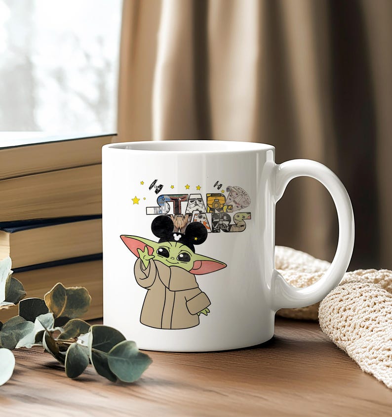 Może przedstawiać: Biały ceramiczny kubek z kresk&oacute;wkowym wizerunkiem Grogu, znanego r&oacute;wnież jako Baby Yoda, w uszach Myszki Miki. Kubek ma logo Gwiezdnych Wojen i inne grafiki związane z Gwiezdnymi Wojnami. Kubek ma duży uchwyt.