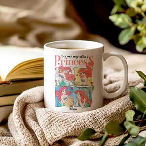 Pode incluir: Caneca de cer&acirc;mica branca com uma ilustra&ccedil;&atilde;o colorida de Ariel de A Pequena Sereia. A caneca tem o texto "N&atilde;o &eacute; f&aacute;cil ser uma princesa".