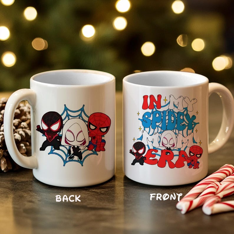 May include: White ceramic mug featuring Spider-Man characters. The back of the mug displays three characters in front of a blue spiderweb design. The front of the mug has the text "IN MY SPIDEY ERA" with character illustrations.