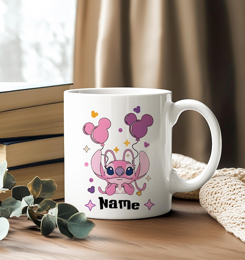 Pu&ograve; includere: Tazza in ceramica bianca con un personaggio dei cartoni animati rosa che tiene in mano palloncini rosa e viola a forma di Topolino. La tazza ha la scritta "Name" in nero, con stelle. Sfondo sfocato.