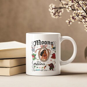 May include: White ceramic coffee mug featuring a colourful illustration of Moana from Disney's Moana. The illustration includes Moana, Maui, Pua the pig, Hei Hei the rooster, and the ocean. The text "Disney Moana Est. 2016" is printed on the mug.
