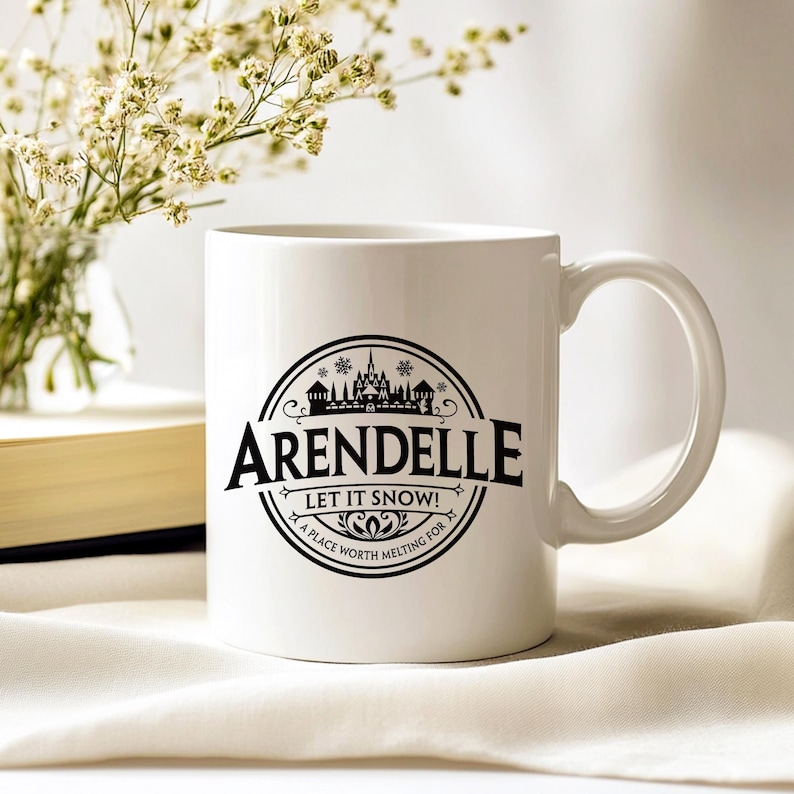 May include: White ceramic mug with a black graphic that reads "Arendelle" with a castle illustration and the text "Let it Snow! A place worth melting for". The mug has a curved handle and is set on a white surface.