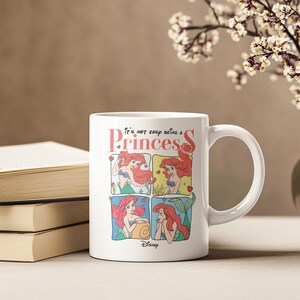 Pode incluir: Caneca de cer&acirc;mica branca com uma ilustra&ccedil;&atilde;o colorida de Ariel de A Pequena Sereia. A caneca tem o texto "It's not easy being a Princess" e o logotipo da Disney.