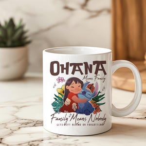 May include: White ceramic mug with a colourful illustration of Lilo and Stitch embracing, and the text "Ohana Means Family" and "Family Means Nobody Gets Left Behind or Forgotten". The mug has a curved handle.