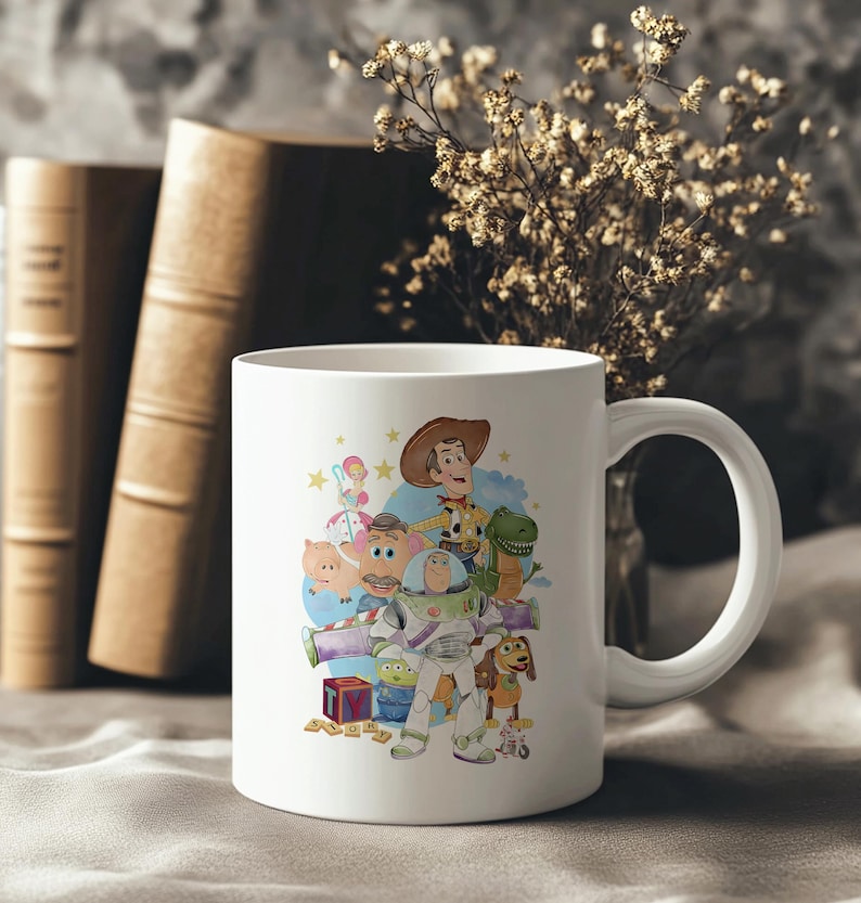 May include: White ceramic mug with a colourful illustration of characters from the animated film Toy Story. The design includes Woody, Buzz Lightyear, Rex, and other characters. The mug has a curved handle and is set against a neutral background.