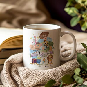 May include: White ceramic mug with a colourful illustration of characters from the animated film Toy Story. The design includes Woody, Buzz Lightyear, and other characters. The mug has a curved handle and is filled with a dark liquid.