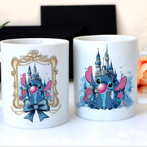 May include: Two white ceramic mugs featuring a blue cartoon character with large ears and a pink bubble. One mug has the character in a gold frame with a blue bow. The other mug has a castle background.