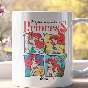 Pode incluir: Caneca de cer&acirc;mica branca com uma ilustra&ccedil;&atilde;o colorida de Ariel de A Pequena Sereia. A caneca apresenta o texto "It's not easy being a Princess" e um logotipo da Disney.
