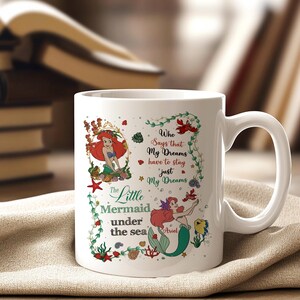 May include: White ceramic mug featuring a colorful illustration of Ariel from The Little Mermaid. The design includes Ariel, sea creatures, and the text "Who Says that My Dreams have to stay just My Dreams".