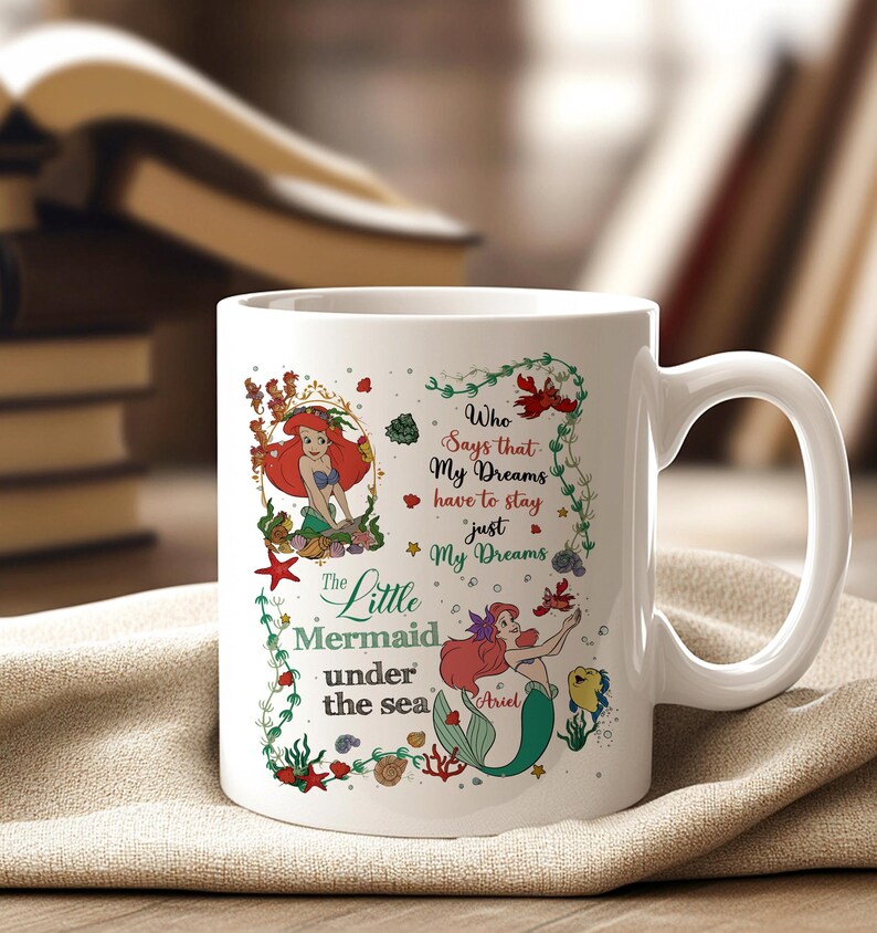 May include: White ceramic mug featuring a colorful illustration of Ariel from The Little Mermaid. The design includes Ariel, sea creatures, and the text "Who Says that My Dreams have to stay just My Dreams".