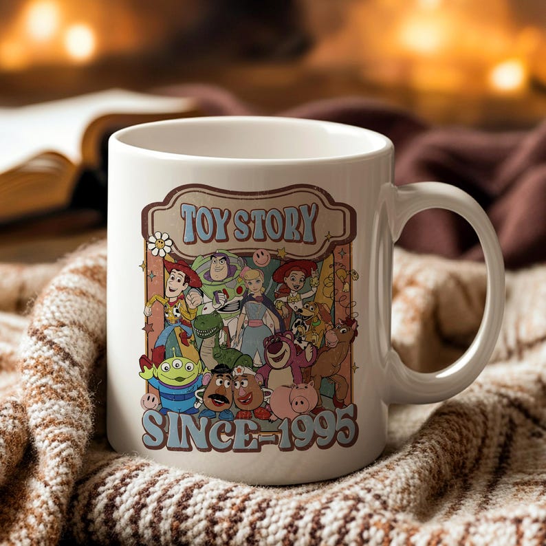 K&ouml;nnte beinhalten: Wei&szlig;e Keramiktasse mit einer farbenfrohen Grafik von Toy Story-Charakteren. Die Tasse tr&auml;gt den Text "TOY STORY" &uuml;ber den Charakteren und "SINCE 1995" darunter. Die Tasse hat einen gebogenen Griff.