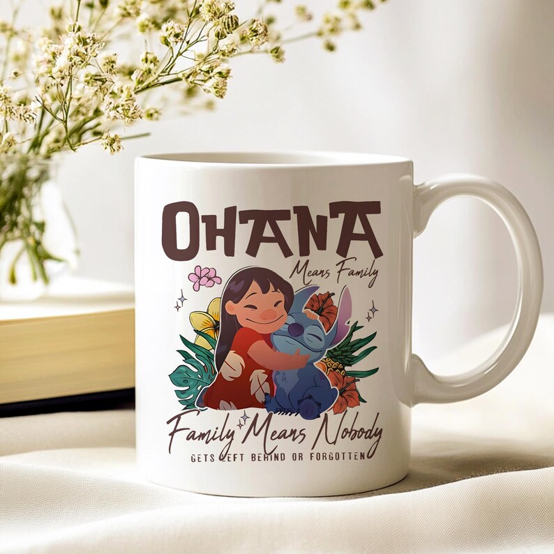 May include: White ceramic mug with a colourful illustration of a girl embracing a blue alien-like creature, with the words "Ohana Means Family" and "Family Means Nobody Gets Left Behind or Forgotten". The mug has a curved handle.