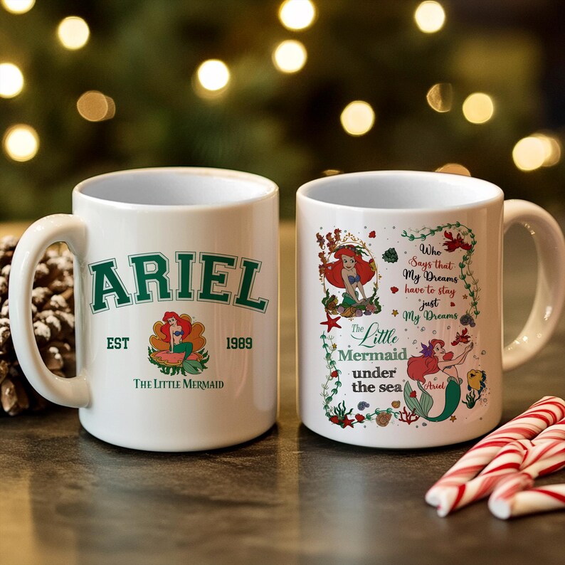 May include: Two white ceramic mugs featuring The Little Mermaid. One mug has "ARIEL" in green, "EST 1989", and a mermaid graphic. The other mug has a mermaid graphic and the text "Who Says that My Dreams have to stay just My Dreams".