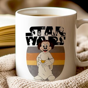 May include: White ceramic mug with a Star Wars logo and a cartoon character dressed as Princess Leia. The character is in a white gown with a gold belt, set against a grey and yellow striped background.