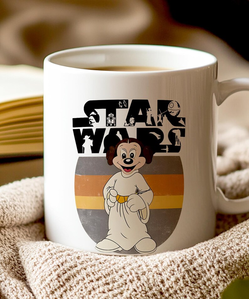 May include: White ceramic mug with a Star Wars logo and a cartoon character dressed as Princess Leia. The character is in a white gown with a gold belt, set against a grey and yellow striped background.