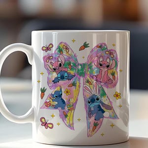 May include: White ceramic mug featuring a colorful bow design with cartoon characters. The bow is decorated with butterflies, carrots, and flowers. The characters are in various poses, some with bunny ears. A fun and whimsical design.