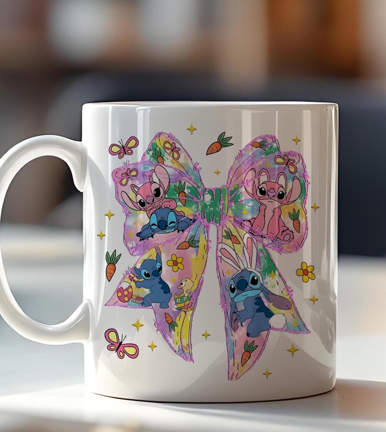 May include: White ceramic mug featuring a colorful bow design with cartoon characters. The bow is decorated with butterflies, carrots, and flowers. The characters are in various poses, some with bunny ears. A fun and whimsical design.