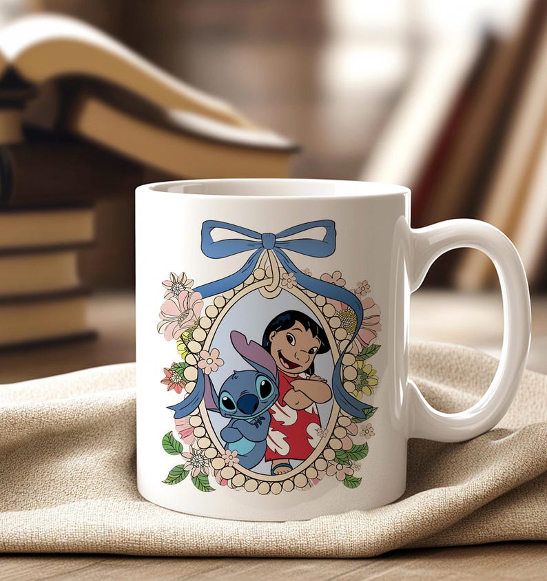 May include: White ceramic mug featuring a colorful illustration of Lilo and Stitch. The design is framed by a blue ribbon and floral accents. The mug has a curved handle and is set against a neutral background.