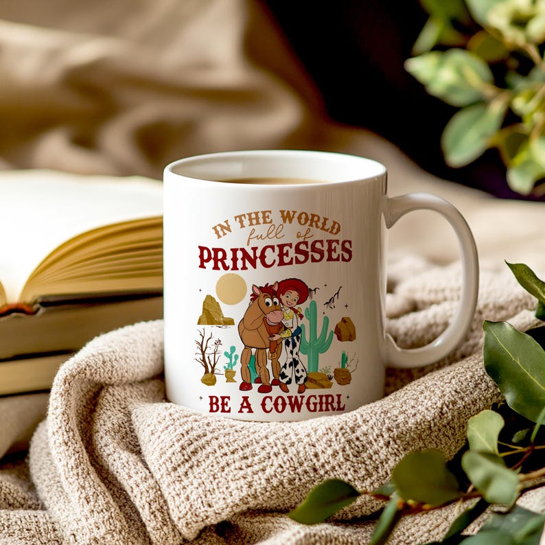 May include: White ceramic mug with a cartoon image of Woody and Bullseye from Toy Story. The mug has the text "In the world full of princesses, be a cowgirl".