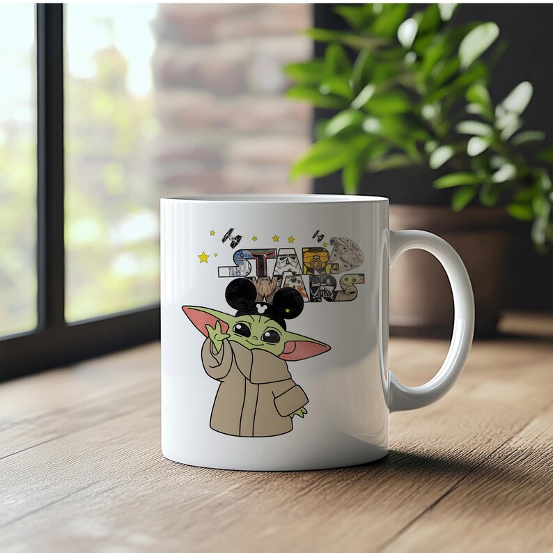 Może przedstawiać: Biały ceramiczny kubek z kresk&oacute;wkowym wizerunkiem Grogu z Gwiezdnych Wojen w uszach Myszki Miki. Kubek ma logo Gwiezdnych Wojen i inne grafiki. Kubek stoi na drewnianej powierzchni.