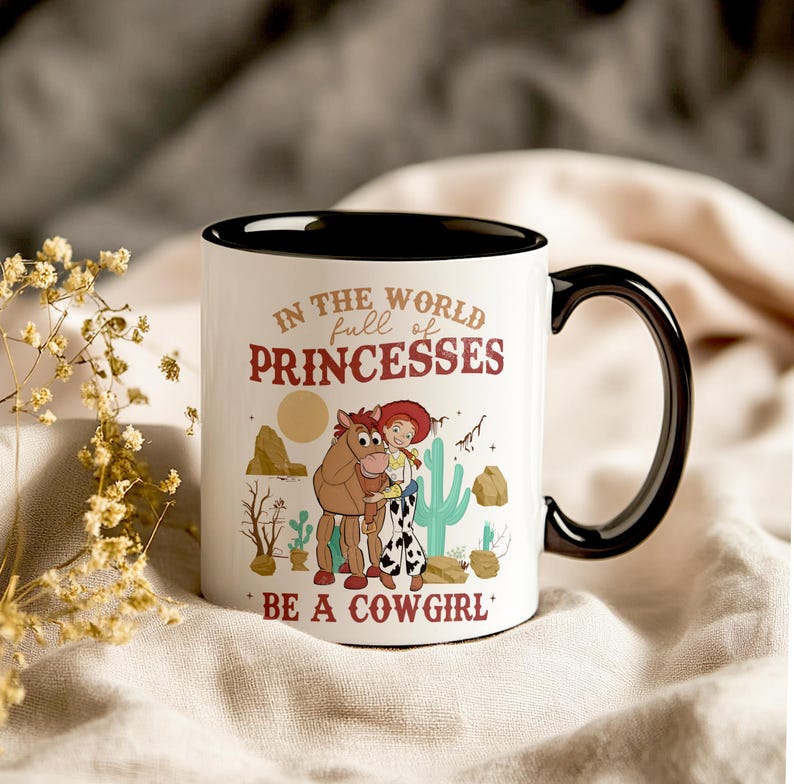 May include: White ceramic mug with a black rim and handle. The mug features a cartoon image of a cowgirl and a horse with the text "In the world full of princesses be a cowgirl".