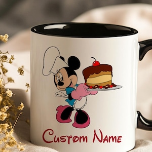 Pu&ograve; includere: Tazza in ceramica bianca con interno e manico neri. La tazza presenta un'illustrazione a cartoni animati di Minnie Mouse con un cappello da chef, che tiene in mano una torta. Le parole "Custom Name" sono stampate in rosso in basso.