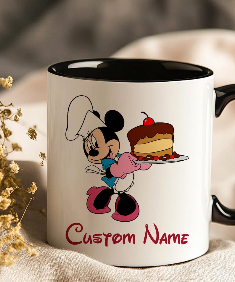 Pu&ograve; includere: Tazza in ceramica bianca con interno e manico neri. La tazza presenta un'illustrazione a cartoni animati di Minnie Mouse con un cappello da chef, che tiene in mano una torta. Le parole "Custom Name" sono stampate in rosso in basso.