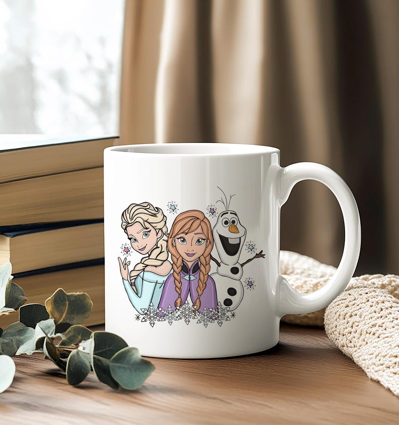 Puede incluir: Taza de cer&aacute;mica blanca con ilustraciones de Elsa, Anna y Olaf de la pel&iacute;cula Frozen. Los personajes est&aacute;n representados con sus trajes caracter&iacute;sticos, con copos de nieve y estrellas. La taza tiene un asa grande.