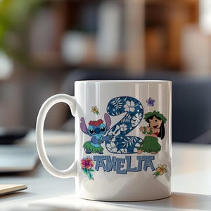 May include: White ceramic mug with a design featuring the number "2" in a blue floral pattern, Stitch, Lilo, and the name "AMELIA". The mug has a curved handle and is decorated with tropical flowers.