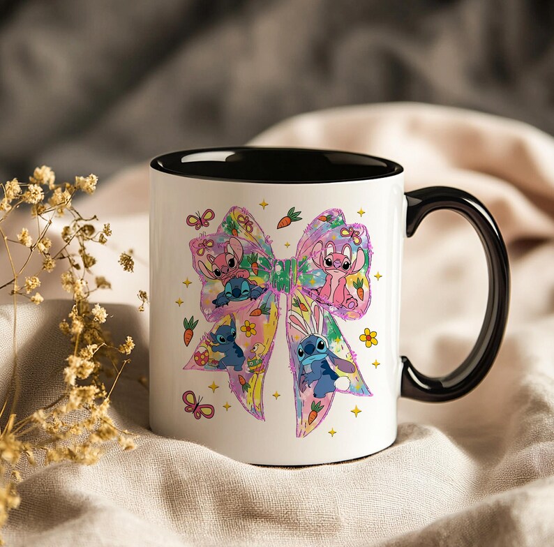 May include: White ceramic mug with a black handle and interior. The mug features a colorful bow design with cartoon characters, flowers, carrots, and butterflies. The design includes pink, blue, yellow, and green elements.