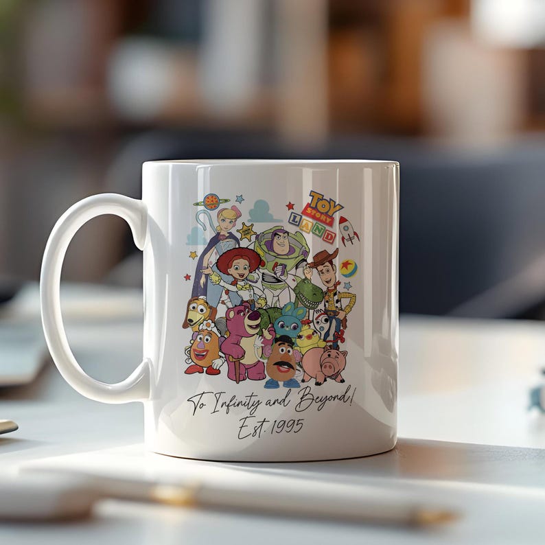Pu&ograve; includere: Una tazza in ceramica bianca con un'illustrazione colorata di personaggi del franchise Toy Story. I personaggi includono Woody, Buzz Lightyear, Jessie e altri. La tazza ha il testo "Toy Story Band" e "To Infinity and Beyond! Est. 1995" stampato su di essa.