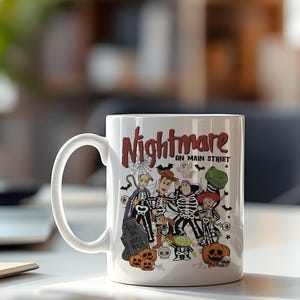 May include: White ceramic mug featuring a Halloween-themed design with the text "Nightmare on Main Street." The design includes cartoon characters dressed in skeleton costumes, pumpkins, and a tombstone. The mug has a large, curved handle.
