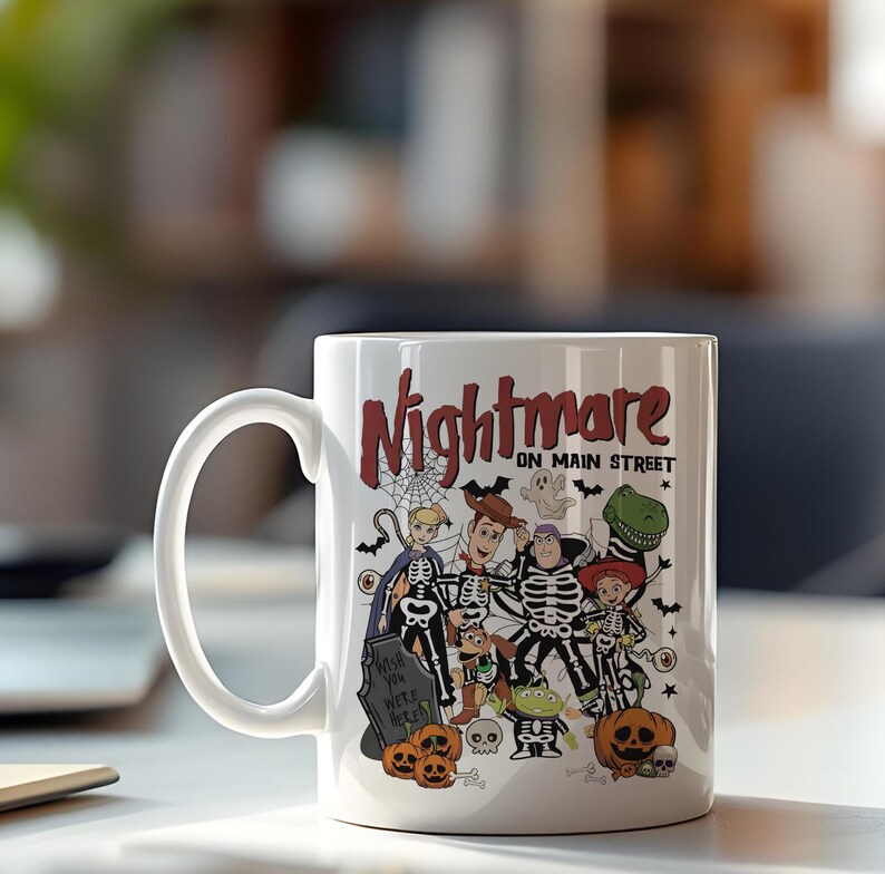 May include: White ceramic mug featuring a Halloween-themed design with the text "Nightmare on Main Street." The design includes cartoon characters dressed in skeleton costumes, pumpkins, and a tombstone. The mug has a large, curved handle.