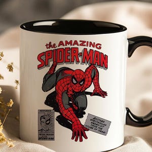 May include: White ceramic mug with a black interior and handle. The mug features a comic book illustration of Spider-Man in red and black, with the text "the AMAZING SPIDER-MAN". Additional text includes "FEATURING" and "PETER PARKER ALIAS SPIDER-MAN".