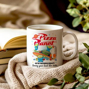 May include: White ceramic mug with a colorful graphic of the Pizza Planet logo and characters from the Toy Story franchise. The text on the mug reads "Pizza Planet", "Out of this world quality", and "Serving your local star cluster".
