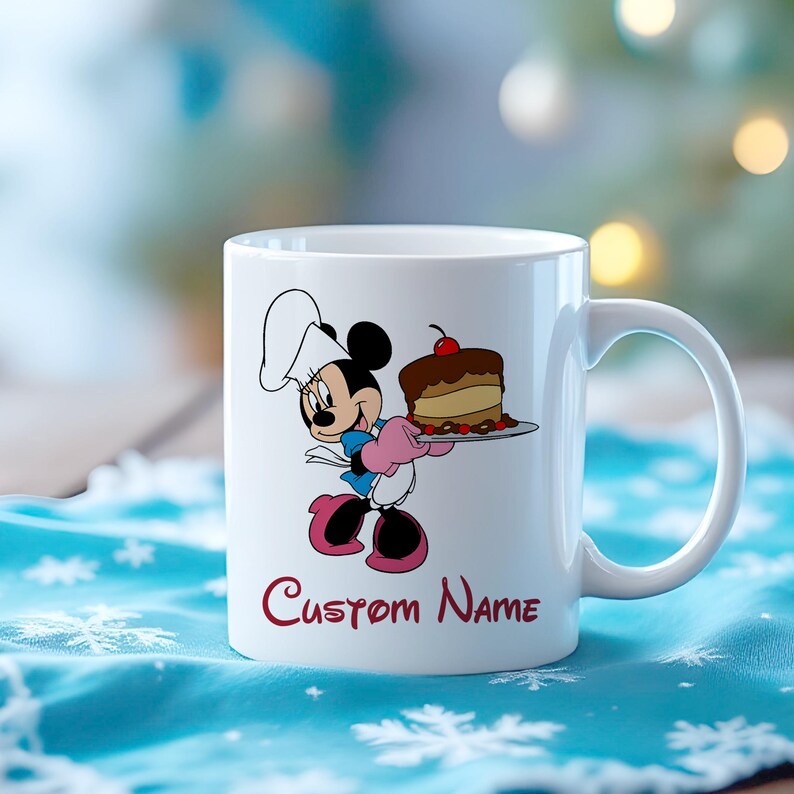 Pu&ograve; includere: Tazza in ceramica bianca con un personaggio dei cartoni animati con un cappello da chef, che tiene in mano una torta su un piatto. La tazza ha un manico curvo e le parole "Custom Name" in corsivo. Il personaggio indossa guanti e scarpe rosa.