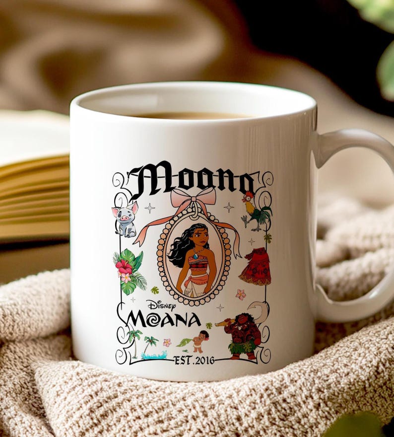 May include: A white ceramic coffee mug with a design featuring Moana from the Disney movie Moana. The design includes Moana in a frame with a pink ribbon, a rooster, a pig, a crab, and a green plant. The text on the mug reads 'Moana', 'Disney Moana', and 'Est. 2016'.