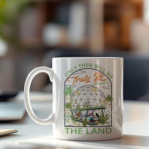 May include: White ceramic mug featuring a colorful graphic of Disney characters in a greenhouse setting, with the text "ONLY THEN WILL WE TRULY BE LIVING WITH THE LAND". The mug has a curved handle.