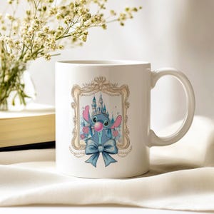 May include: White ceramic mug featuring a cartoon character with a blue body, pink ears, and a bubblegum bubble. The character is framed by a gold-colored ornate border with a castle backdrop and a blue bow. The mug has a curved handle.