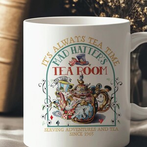 Puede incluir: Taza de cer&aacute;mica blanca con una colorida ilustraci&oacute;n de una tetera, un reloj y naipes. La taza tiene el texto "It's Always Tea Time, Mad Hatter's Tea Room, Serving Adventures and Tea Since 1965."