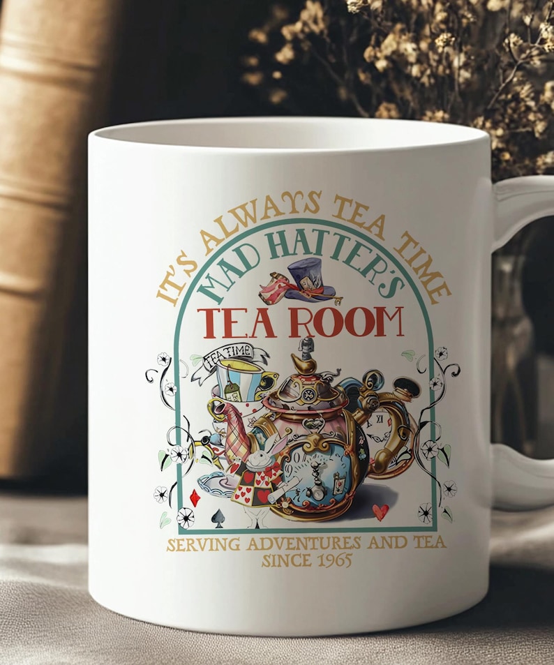 Puede incluir: Taza de cer&aacute;mica blanca con una colorida ilustraci&oacute;n de una tetera, un reloj y naipes. La taza tiene el texto "It's Always Tea Time, Mad Hatter's Tea Room, Serving Adventures and Tea Since 1965."