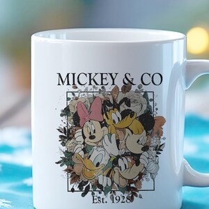 May include: White ceramic mug with a floral design featuring Mickey Mouse, Minnie Mouse, Donald Duck, and Goofy. The text "Mickey & Co. Est. 1928" is printed on the mug.