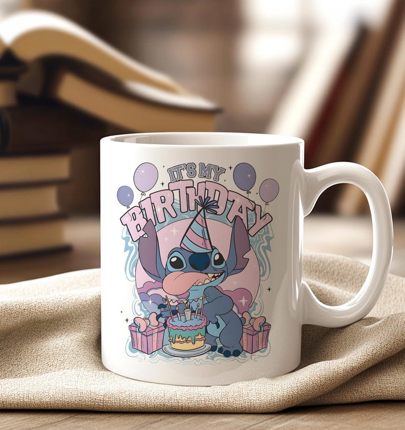 May include: White ceramic mug featuring a cartoon character with the text "IT'S MY BIRTHDAY". The character is blue with large ears and is wearing a party hat. The mug also has a birthday cake and presents.